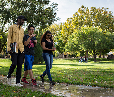 Students are walking on campus after a rain storm. Trees are in the background.
